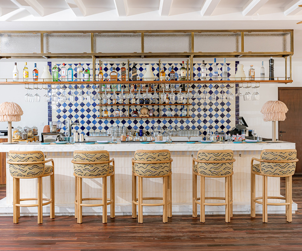 Five light wood James Bar Chairs with patterned fabric seats arranged in front of a bright marble counter at Blu Beach Bar & Grill.