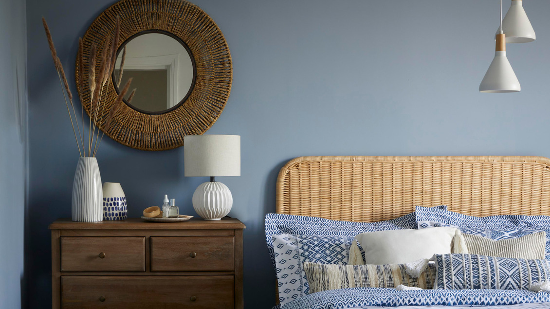 Coastal Grandma Style Home bedroom featuring a minimalist design with a rattan headboard and matching rattan mirror."