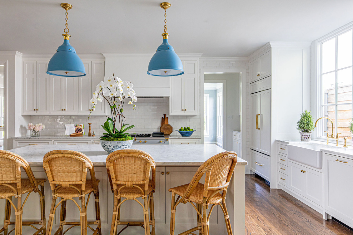 Coastal Grandma Style Home kitchen featuring white cabinetry, marble countertops, and rattan bar chairs.