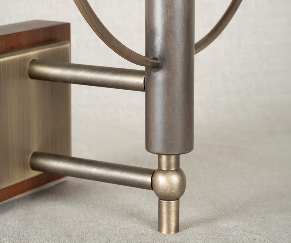 Close-up detail of the Faraday Wall Lamp base by Wood Tailors Club, focusing on the aged brushed brass dual-arm structure and the smoked walnut backplate mounting.
