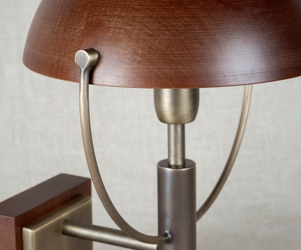 Close-up detail of the top section of the Faraday Wall Lamp by Wood Tailors Club, highlighting the aged brushed brass joints and the texture of the smoked walnut dome shade.