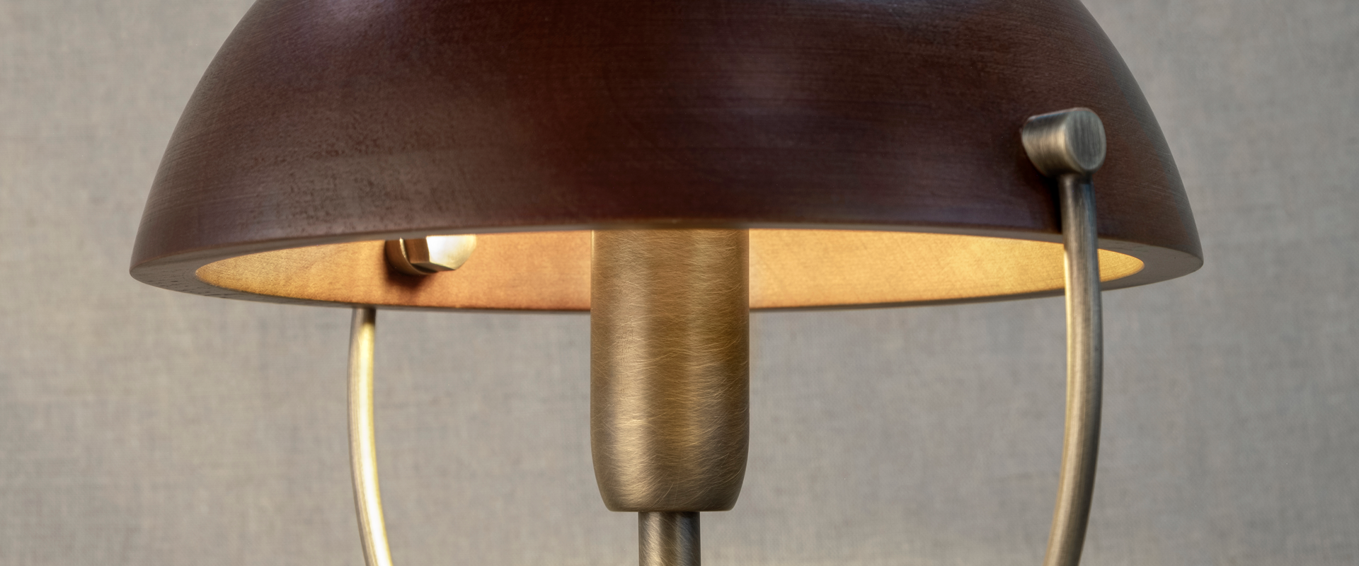Close-up of the Faraday Wall Lamp by Wood Tailors Club, showcasing the interior of its smoked walnut domed shade softly illuminated, revealing the aged brushed brass socket and metal ring structure.