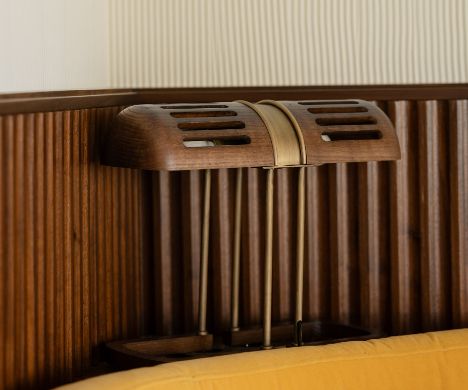 Close-up side view of the Turing Table Lamp with a slatted wooden shade and brass accents, placed next to a ribbed wood wall panel at Pool House by Studio Quentin, Monte-Carlo, Monaco