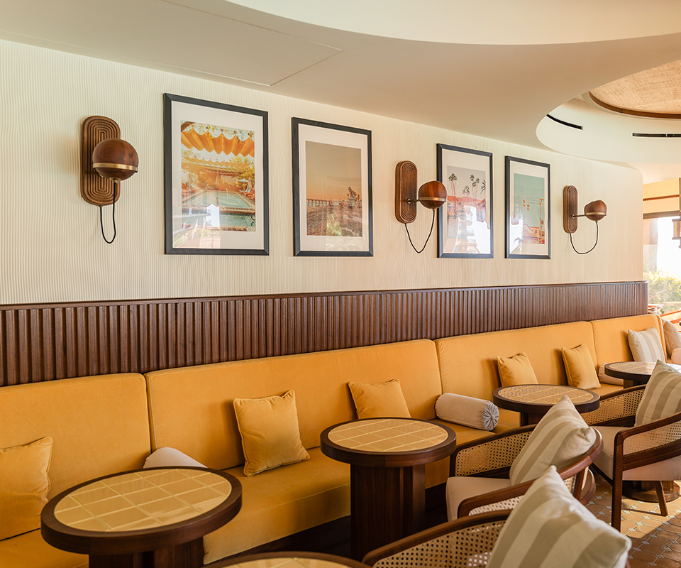 Several Fleming Wall Lamps are mounted on the wall above a long yellow velvet sofa in this restaurant space at Pool House by Studio Quentin, Monte-Carlo, Monaco