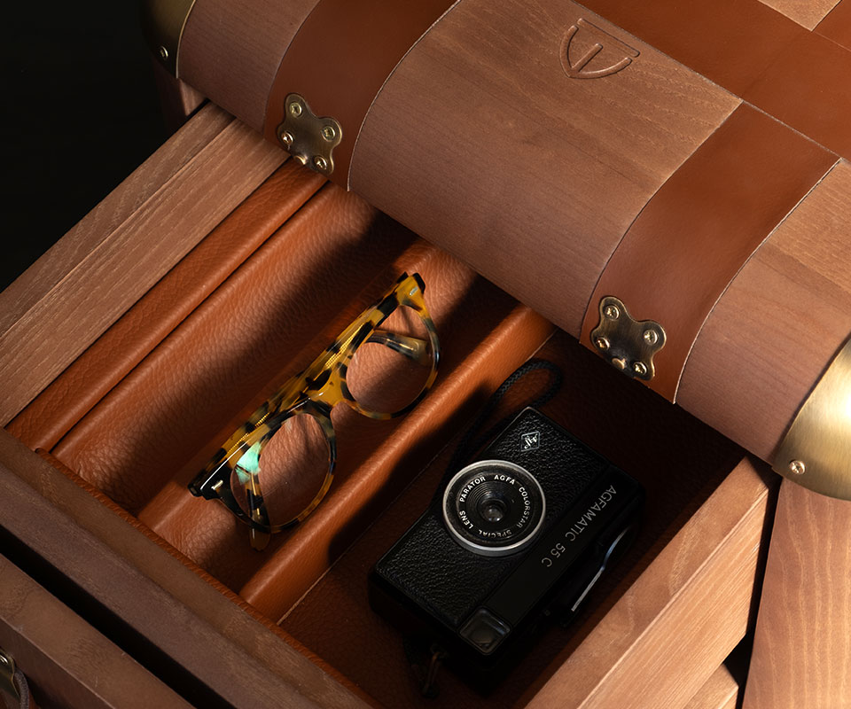 Burke Side Table Close-up of the Burke side table showcasing the drawers’ leather interior with a vintage camera and glasses inside. The tabletop features the Wood Tailors Club brand icon engraved in the wood.