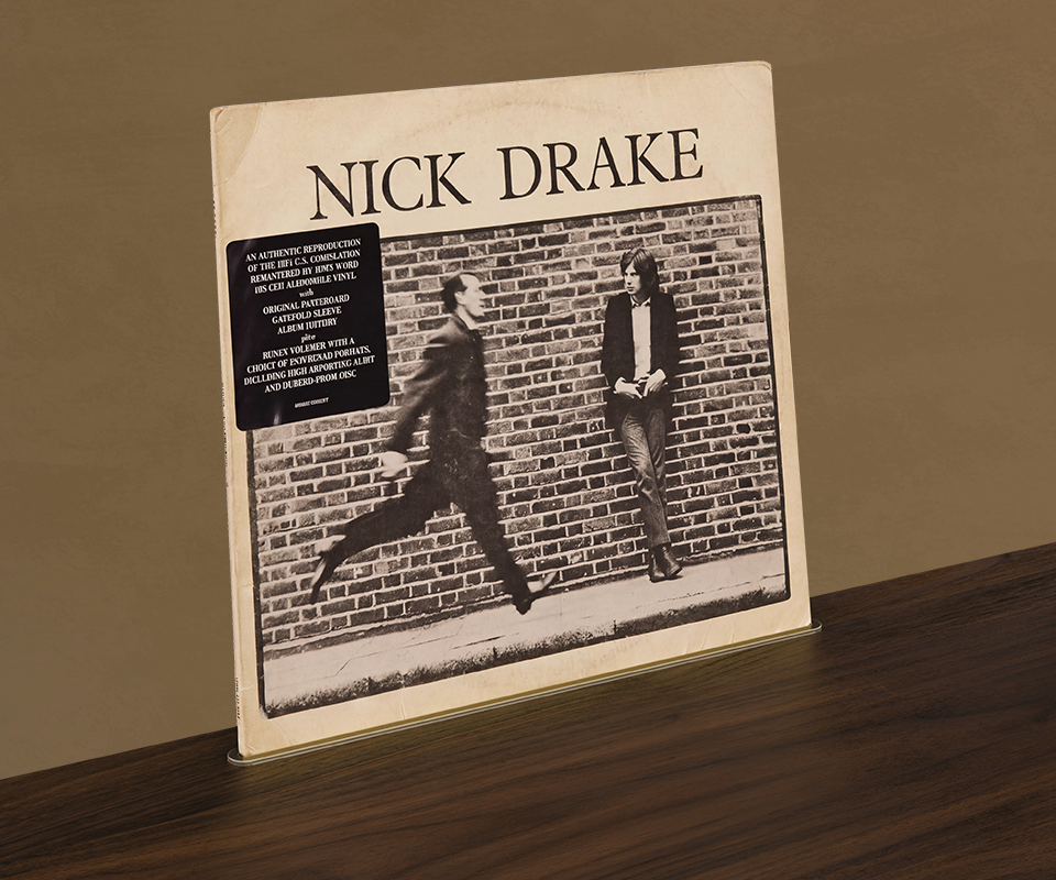 Close-up of a vinyl record album standing upright in a brass track holder on the wooden top surface of the Edward Sideboard by Wood Tailors Club.