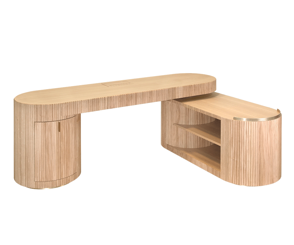 Gifford Desk Gifford desk by Wood Tailors Club in oak. An angled perspective view of the desk in an L-shaped arrangement. It features an oak fluted-panel cabinet on the left, supporting the main oak top, and a lower oak shelf module with two open shelves extended to the right, finished with a brass trim.
