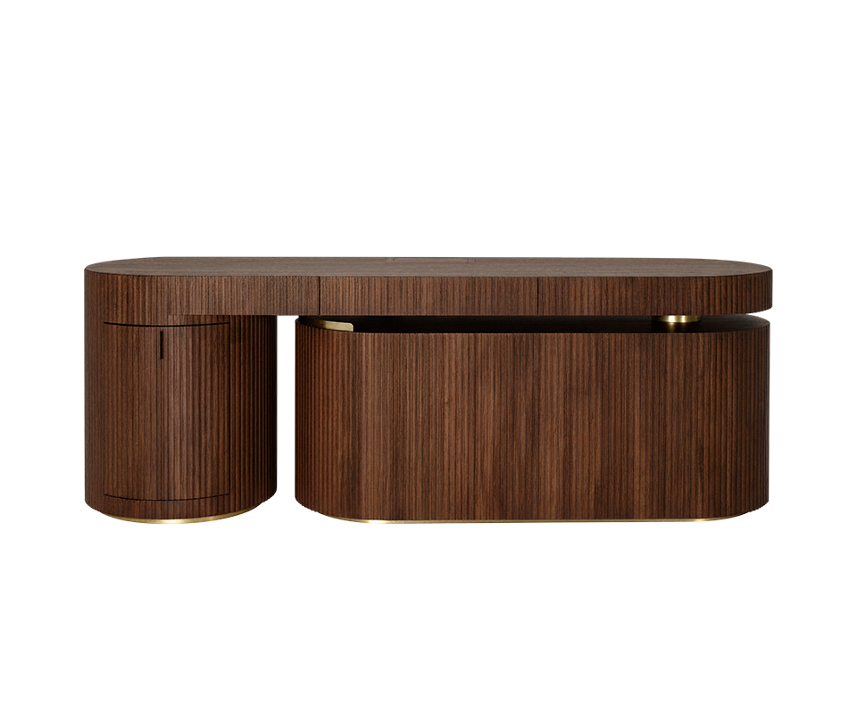 Gifford Desk Gifford desk by Wood Tailors Club in smoked walnut wood. Front view of the desk in a linear, closed configuration. The lower dark wood shelf module is retracted parallel to the main dark wood desktop, with its curved, closed fluted side facing forward, to the right of the fluted dark wood cabinet on the far left. Polished brass leg details.
