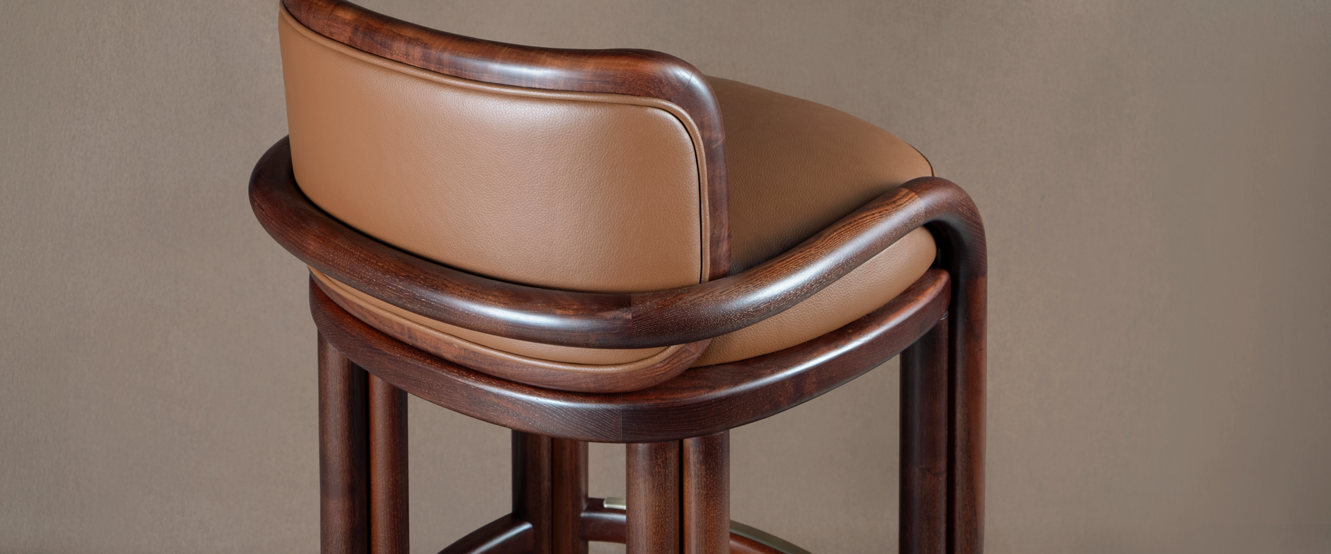 Close-up detail shot of the James Bar Chair showing the curved smoked walnut wood joint structure and fine tan genuine leather upholstery.