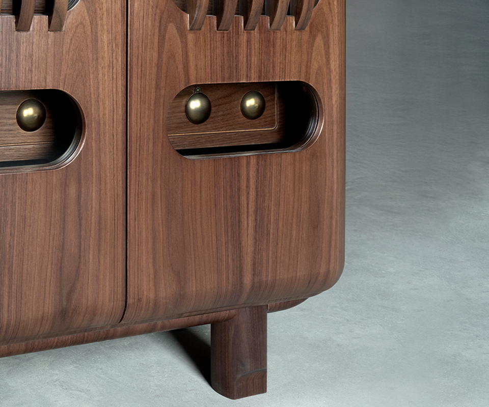 Kennedy Golf Locker A close-up shot of the lower section of the smoked walnut locker. It shows the curved bottom corner, a sturdy square leg, and a recessed handle area on the door featuring spherical details made of aged brushed brass.
