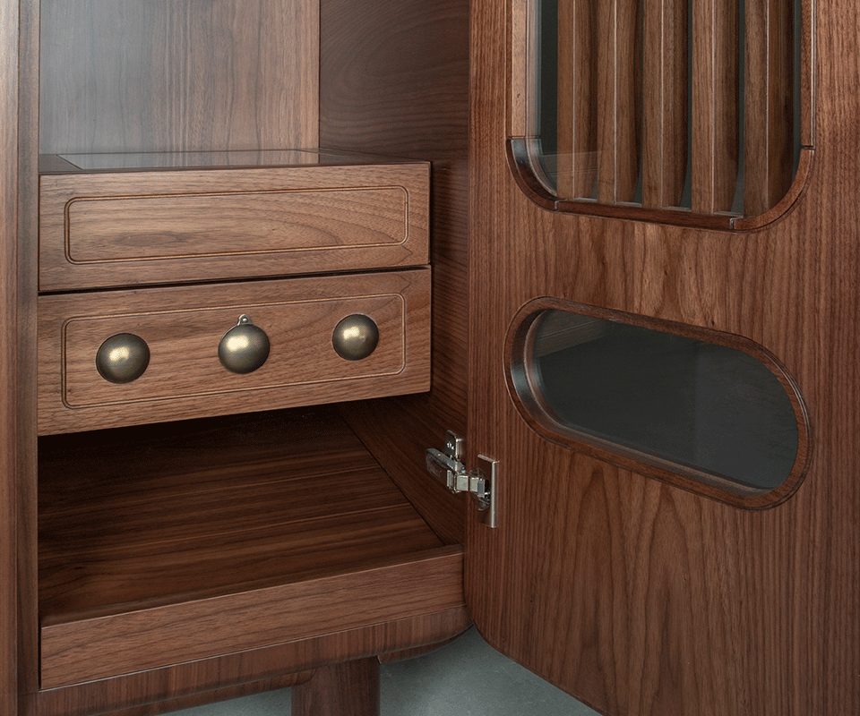Kennedy Golf Locker Close-up of the interior lower right corner. It displays a bespoke drawer front in smoked walnut with three spherical aged brushed brass details, positioned next to the open door which contains a glass-protected slatted window.