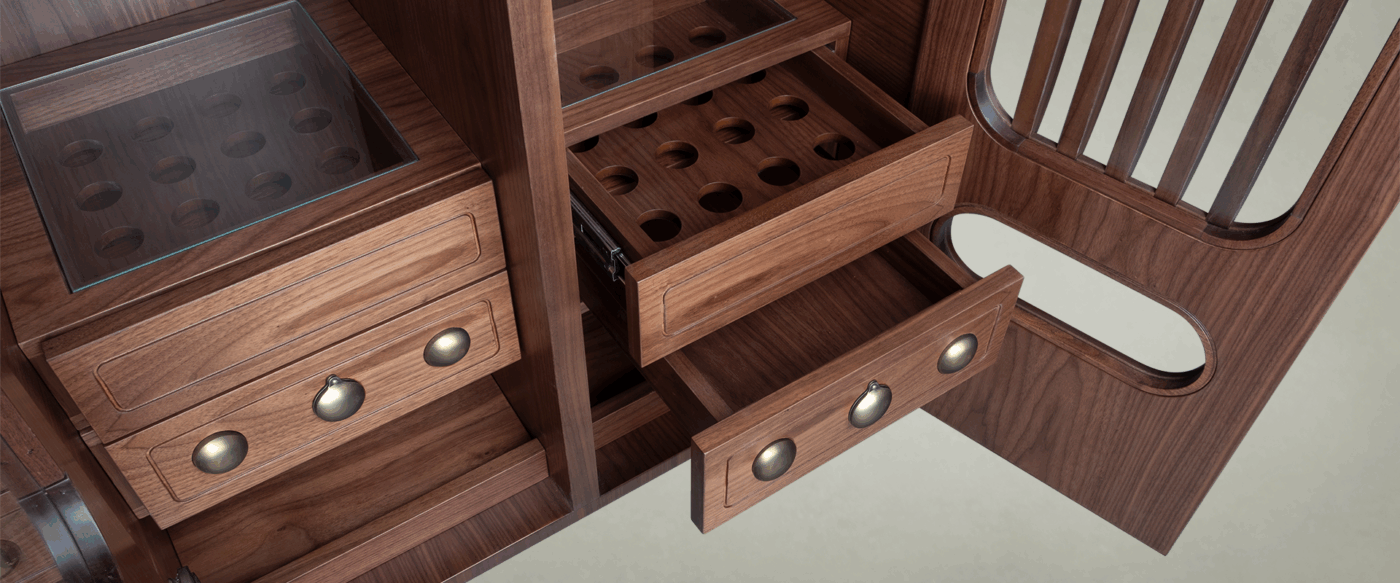Kennedy Golf Locker A high-angle close-up of the internal drawer system in smoked walnut wood. The image shows one drawer partially extended, revealing a bespoke wooden grid with circular cutouts designed to hold golf balls. The drawers are finished with spherical aged brushed brass details, and the top compartments are covered with protective glass panels.