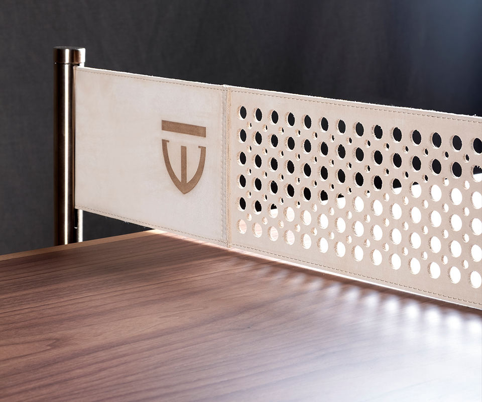 Detailed close-up of a luxury ping pong table made of smooth walnut wood, featuring a custom off-white perforated leather net with the Wood Tailors Club crest embossed on the side, anchored by a sleek stainless steel post.