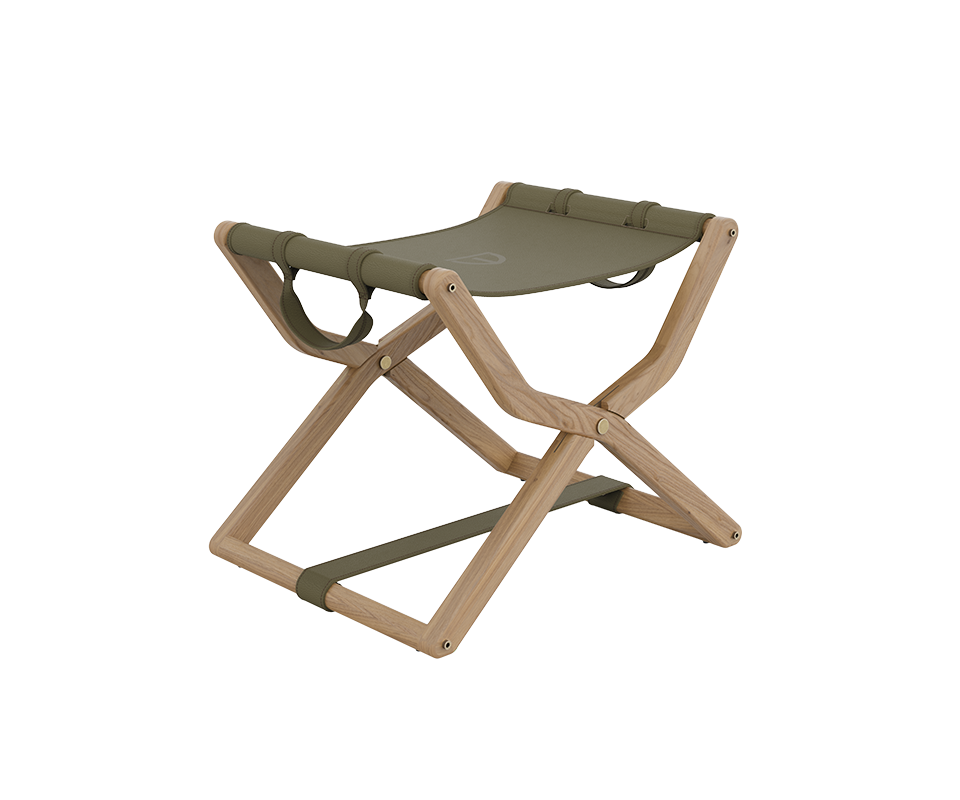 Three-quarter view of the Korda Folding Stool featuring a light-toned oak wood frame with visible grain. The seat is crafted from olive green leather, secured with matching straps and refined brass hardware.