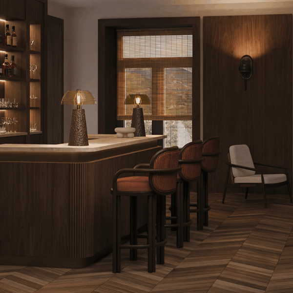 A sophisticated bar lounge with warm wood paneling, chevron wooden flooring, and elegant bar stools. Two Lloyd I Table Lamps with ribbed glass shades and textured dark wood bases illuminate the marble counter.