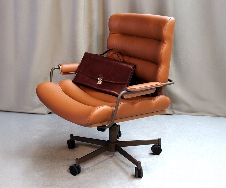 Thomas I Office Chair Thomas I office chair in orange genuine leather, paired with smoked walnut wood, powder-coated stainless steel, and lacquered wood, shown in a setting with a work briefcase.
